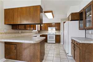Kitchen with kitchen peninsula, white appliances, light tile flooring, tasteful backsplash, and sink