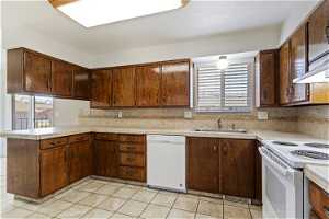 Kitchen featuring kitchen peninsula, white appliances, light tile flooring, tasteful backsplash, and sink