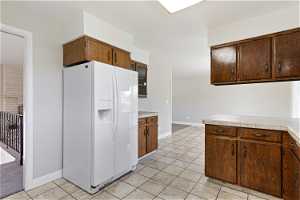 Kitchen featuring brick wall, tile countertops, light carpet, and white refrigerator with ice dispenser