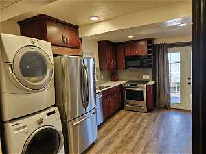 CASIA-featuring backsplash, stainless steel appliances, stacked washer / drying machine, a textured ceiling, and light wood-type flooring