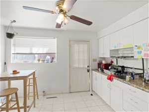 Kitchen featuring ceiling fan, white cabinetry, light tile floors, and light stone counters
