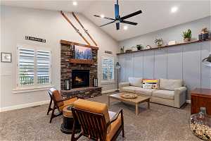Living room featuring a stone fireplace, high vaulted ceiling, ceiling fan, and carpet floors