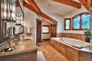 Bathroom with tiled bath, vanity, lofted ceiling with beams, and tile flooring