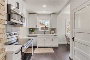 Kitchen with a healthy amount of sunlight, tasteful backsplash, electric stove, and white cabinets