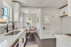 Kitchen featuring plenty of natural light, white cabinets, decorative light fixtures, and tasteful backsplash