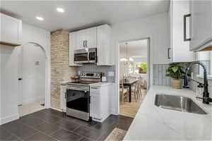 Kitchen with stainless steel appliances, tasteful backsplash, dark tile flooring, white cabinetry, and sink