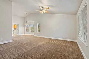 Unfurnished living room featuring ceiling fan with notable chandelier, vaulted ceiling, and light carpet