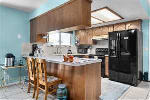 Kitchen with sink, kitchen peninsula, light tile flooring, and black appliances