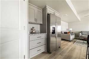 Interior space featuring light hardwood / wood-style flooring, stainless steel refrigerator with ice dispenser, light stone countertops, and gray cabinetry