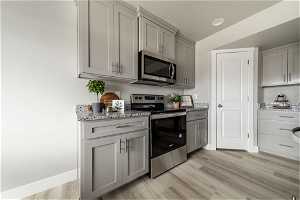 Kitchen with gray cabinets, light stone counters, appliances with stainless steel finishes, and light wood-type flooring