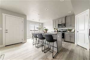 Kitchen with gray cabinets, a center island with sink, light hardwood / wood-style floors, and decorative light fixtures