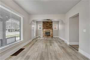 Unfurnished living room with light hardwood / wood-style flooring, ceiling fan, and a stone fireplace