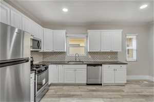Kitchen with a healthy amount of sunlight, appliances with stainless steel finishes, white cabinetry, and sink