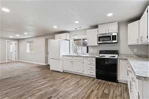 Kitchen featuring light colored carpet, light stone countertops, white appliances, white cabinets, and sink