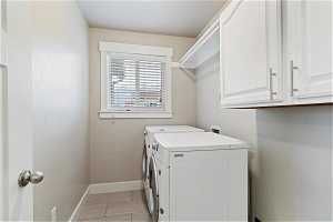 Laundry room featuring cabinets, washing machine and dryer, and light tile floors
