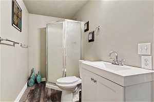 Bathroom with vanity, a textured ceiling, toilet, hardwood / wood-style flooring, and a shower with door