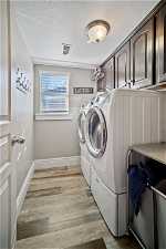 Clothes washing area with cabinets, washer and dryer, light wood-type flooring, and a textured ceiling