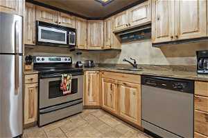 Kitchen with appliances with stainless steel finishes, sink, dark stone counters, and light tile floors