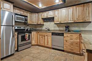Kitchen featuring light tile floors, sink, wood ceiling, stainless steel appliances, and light stone countertops