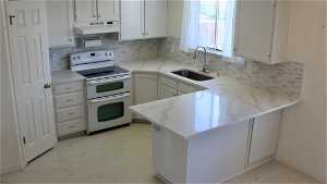 Kitchen with quartz counters, range hood, sink, white cabinets, and range with double oven oven