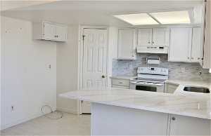 Kitchen with quartz counters, range hood, sink, white cabinets, and range with double oven oven