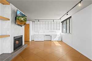 Unfurnished living room with a fireplace, track lighting, and light tile flooring