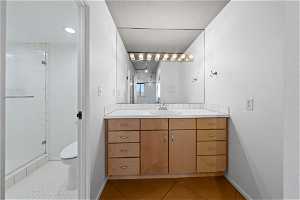 Bathroom featuring large vanity, a shower with shower door, toilet, and tile flooring