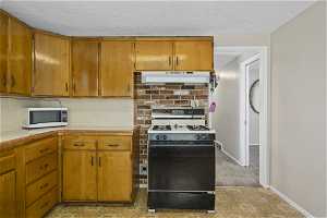 Kitchen featuring a textured ceiling, appliances, tasteful backsplash, light colored carpet, and extractor fan