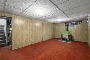 Basement with wood walls, a wood stove, and carpet flooring