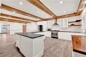 Kitchen featuring wall chimney exhaust hood, white cabinets, sink, light hardwood / wood-style floors, and stainless steel appliances