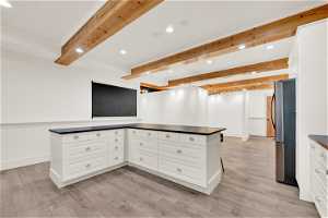 Kitchen featuring beamed ceiling, stainless steel refrigerator, light wood-type flooring, and white cabinets