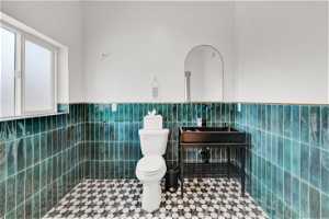 Bathroom featuring toilet, tile floors, tile walls, and sink