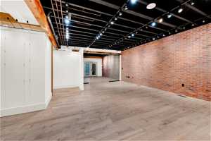 Main level with light hardwood / wood-style floors, brick wall, and rail lighting