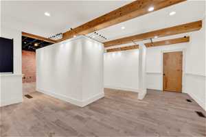 Interior space with light hardwood / wood-style flooring, beam ceiling, and brick wall