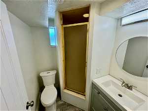 Bathroom featuring walk in shower, a textured ceiling, vanity, and toilet