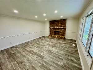 Unfurnished living room featuring hardwood / wood-style flooring, brick wall, a brick fireplace, and ornamental molding