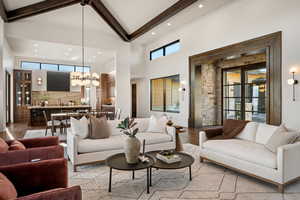 Living room featuring a high ceiling, a chandelier, plenty of natural light, wood finished floors, and beam ceiling
