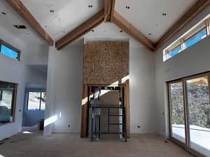 Unfurnished living room featuring beamed ceiling and a towering ceiling