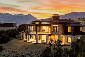 Back of house at dusk featuring a mountain view, stone siding, a patio, a balcony, and a chimney