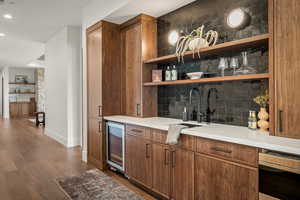 Bar featuring brown cabinets, open shelves, light stone counters, dark wood-style floors, and wine cooler