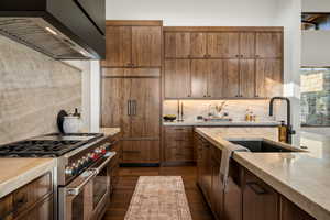 Kitchen featuring range with two ovens, premium range hood, backsplash, paneled refrigerator, and light stone countertops