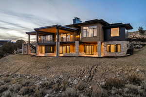 Rear view of house with stone siding, a patio area, a chimney, a balcony, and stairway