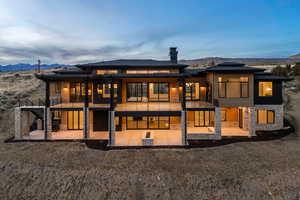 Back of house at dusk featuring stone siding, a patio, a mountain view, and a chimney