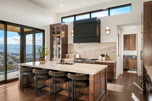 Kitchen with backsplash, a kitchen bar, brown cabinets, light stone counters, and wall chimney exhaust hood