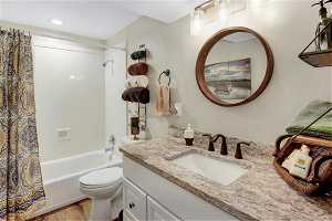 Full bathroom with hardwood / wood-style flooring, shower / bathtub combination with curtain, toilet, and large vanity
