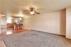 Unfurnished living room featuring ceiling fan and dark carpet