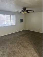Unfurnished room with a textured ceiling, a wall mounted AC, ceiling fan, and dark colored carpet