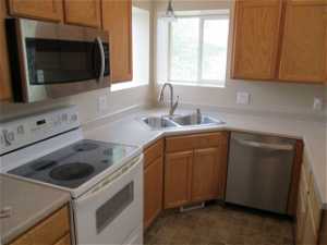 Kitchen featuring dark tile floors, appliances with stainless steel finishes, decorative light fixtures, and sink