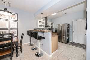 Kitchen with light tile floors, a kitchen bar, stainless steel refrigerator, kitchen peninsula, and pendant lighting