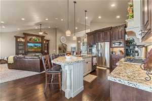 Kitchen with a breakfast bar area, dark hardwood / wood-style flooring, stainless steel appliances, a kitchen island with sink, and light stone countertops